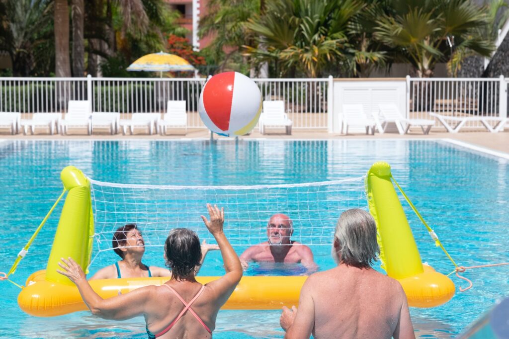 Group of seniors playing in swimming pool with floating volleyball net and ball while enjoy vacation